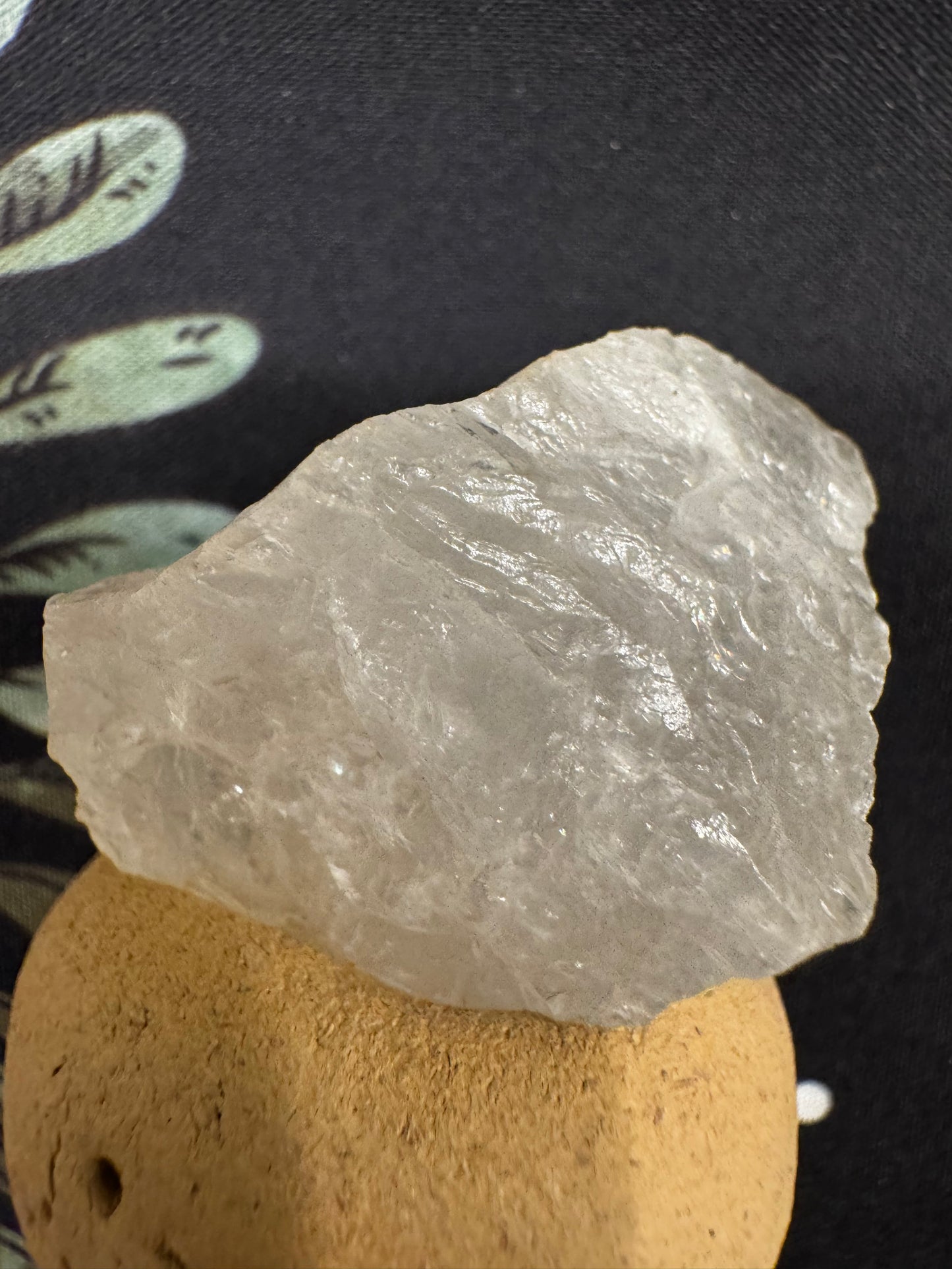 A clear quartz crystal rests on a round, light brown base against a black patterned background.