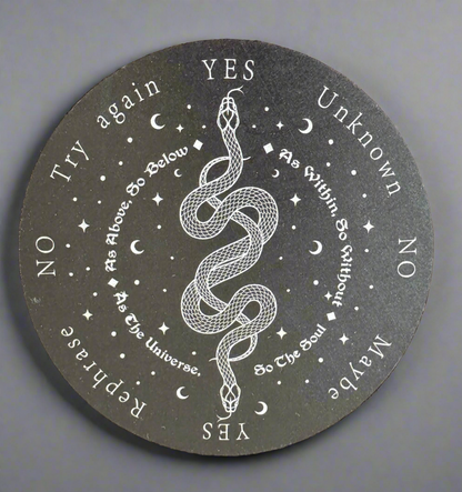 Close-up of a dark, round divination board with white lettering, featuring a snake coiled in the center.