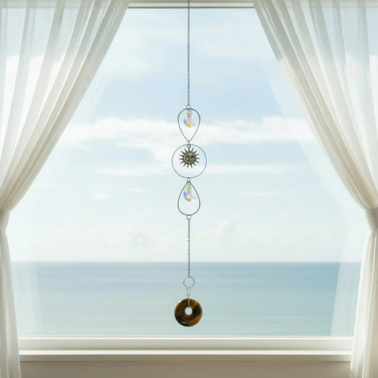 Pretty Tigers Eye crystal suncatcher with silver accents, charms in a window with the sea behind it
