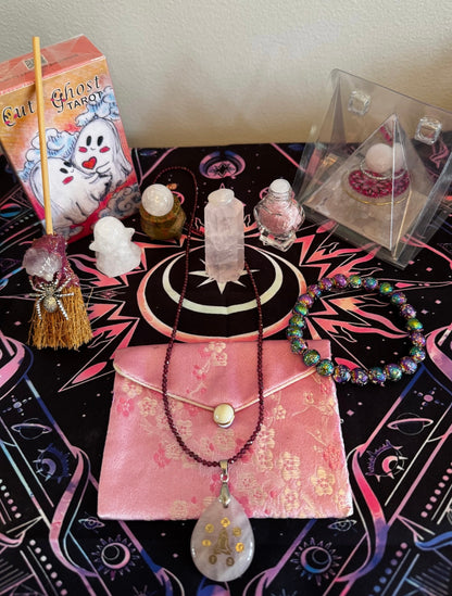 Product display featuring a tarot deck, crystals, jewelry, and other spiritual items arranged on a patterned tablecloth.