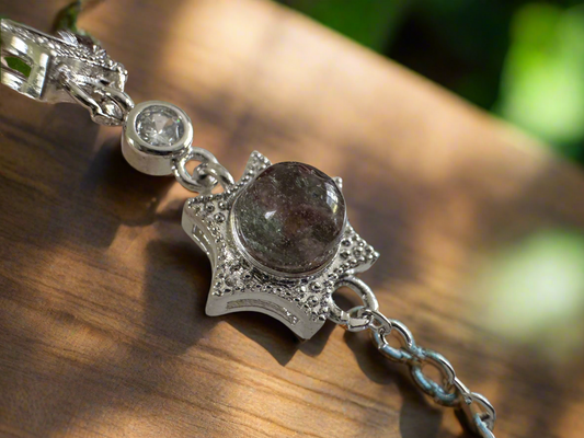 Close-up of a silver star bracelet featuring a dark, speckled gem, resting on a wooden surface.