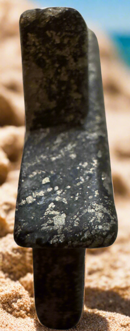 Close-up of a polished, dark green stone axe on a sandy surface.