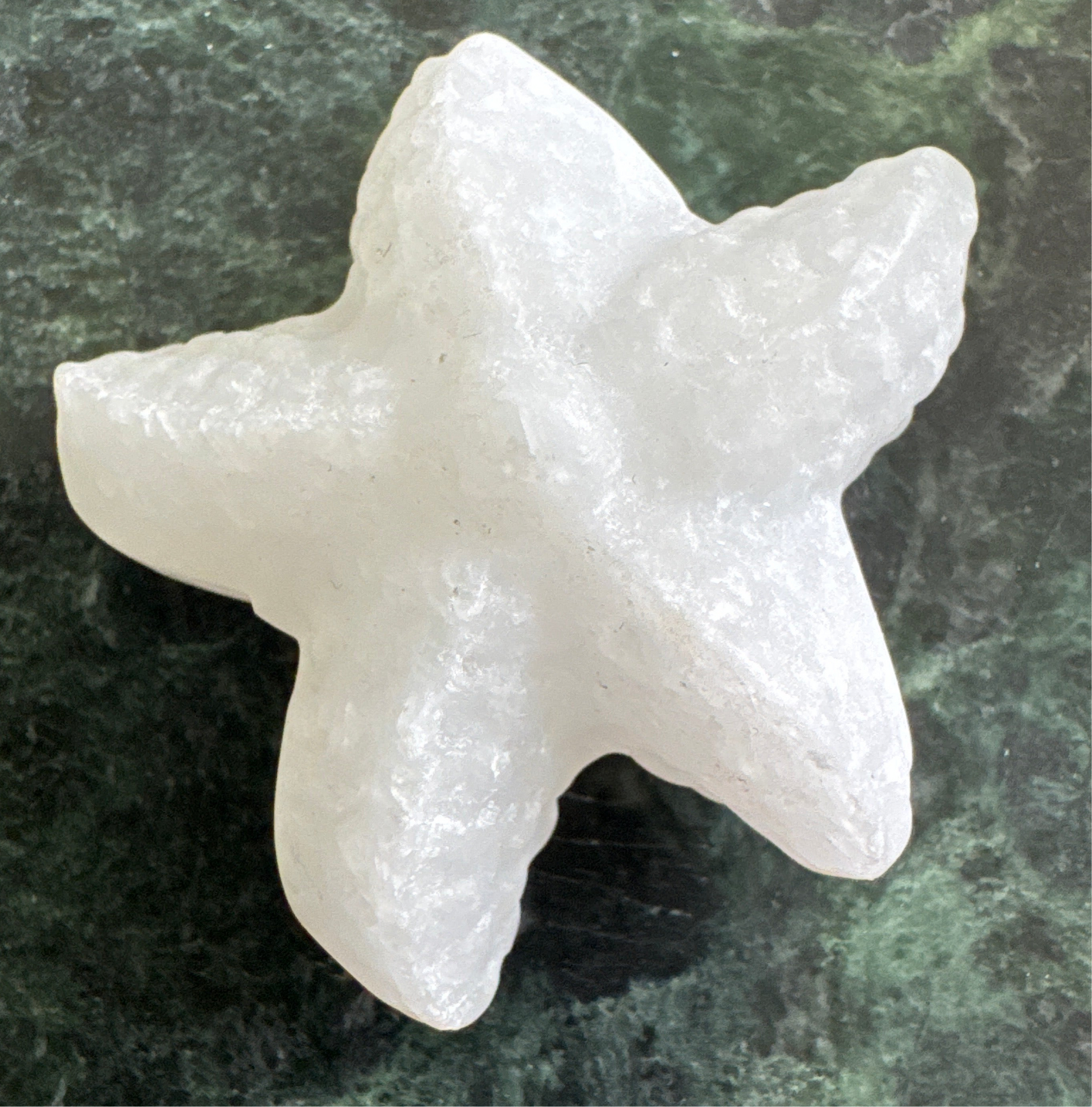 White, roughly shaped, stone starfish on mottled green surface.