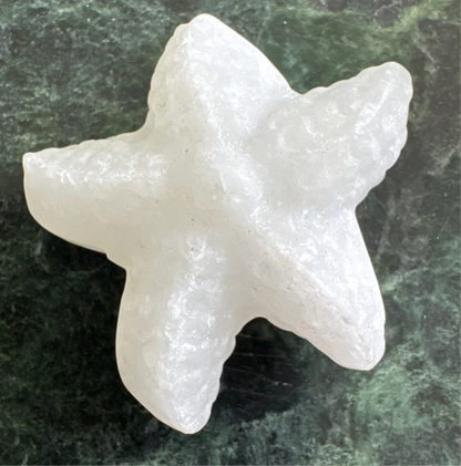 White, roughly shaped, stone starfish on mottled green surface.