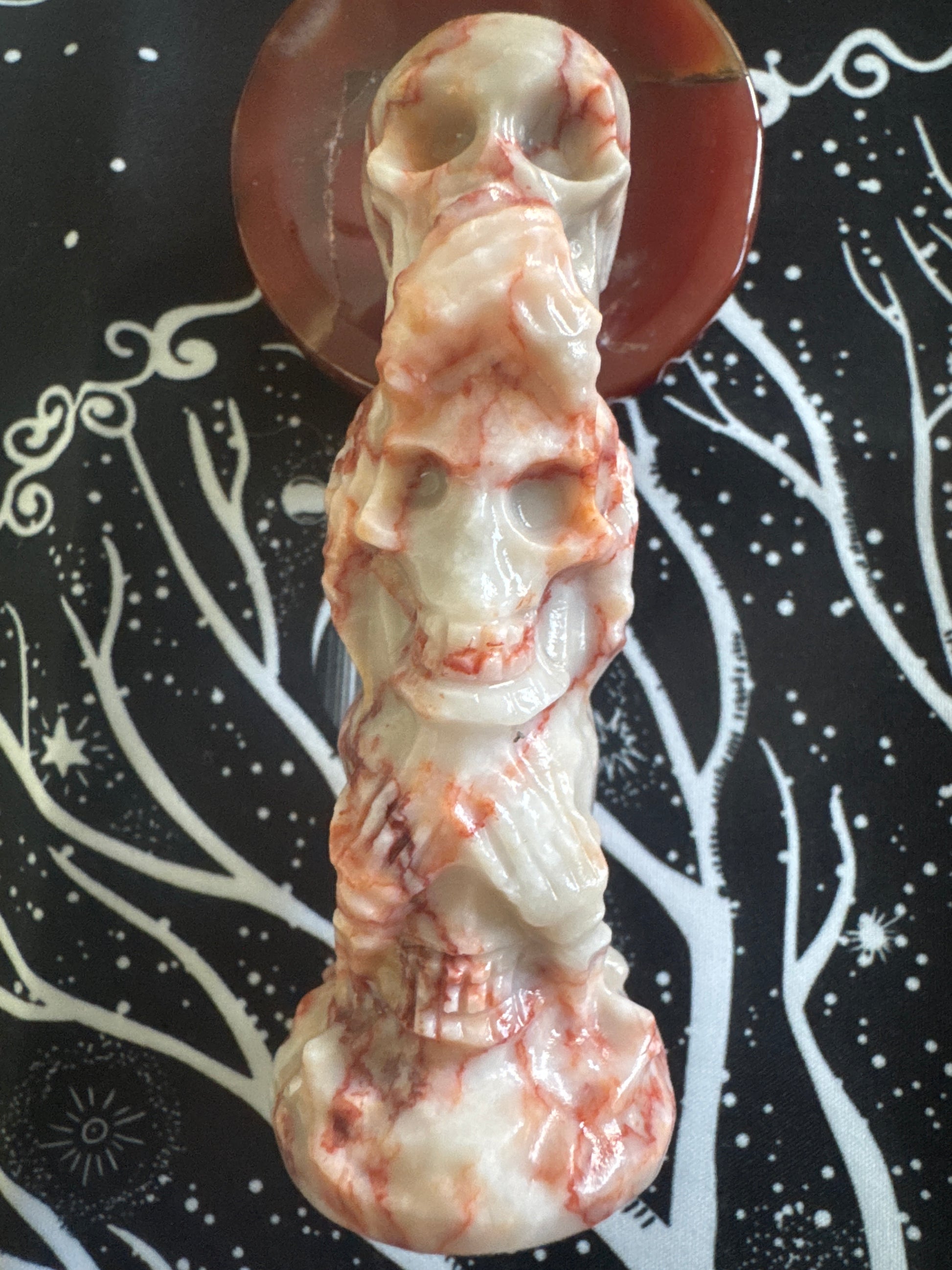 Tumbled rose quartz crystal skull tower on a red agate base, against a black fabric background with white tree and star patterns.