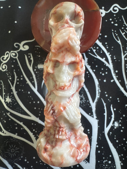Tumbled rose quartz crystal skull tower on a red agate base, against a black fabric background with white tree and star patterns.