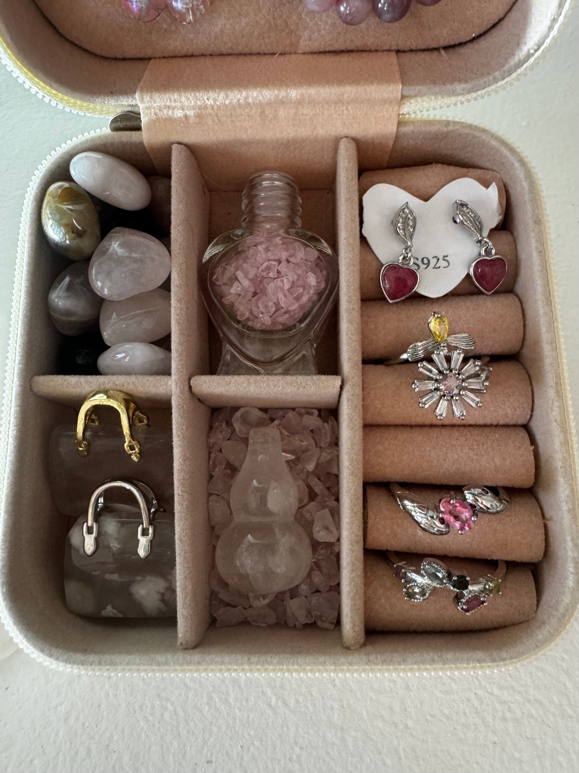 Open jewelry box with pink velvet interior holding jewelry, polished stones, and a perfume bottle filled with pink chips. 
