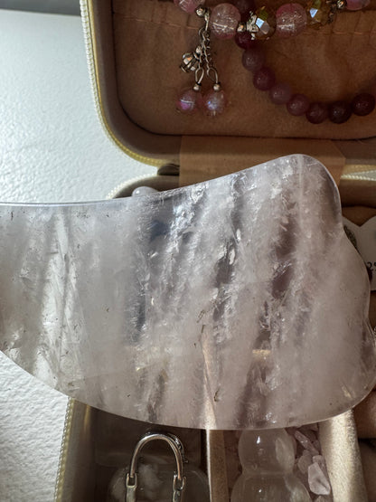 Close-up of a rose quartz gua sha tool in a jewelry box next to a pink beaded bracelet.