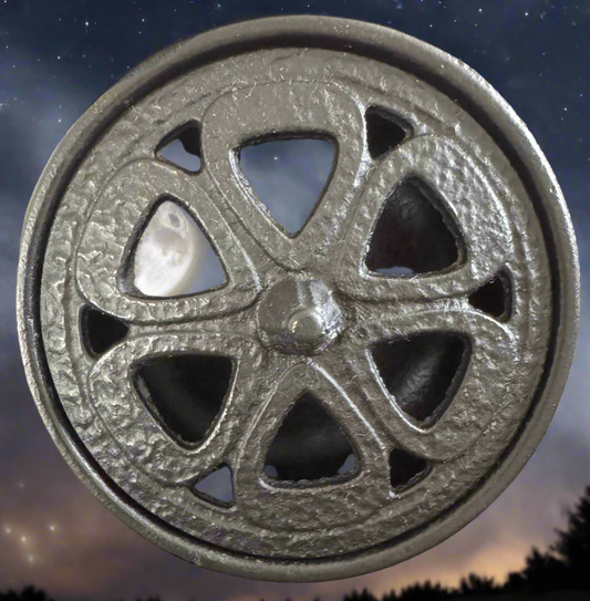 A small, black cast iron cauldron with a decorative pentacle design on the lid and three legs, displayed from over head angle with stars background Main Street Crystals and Minerals 