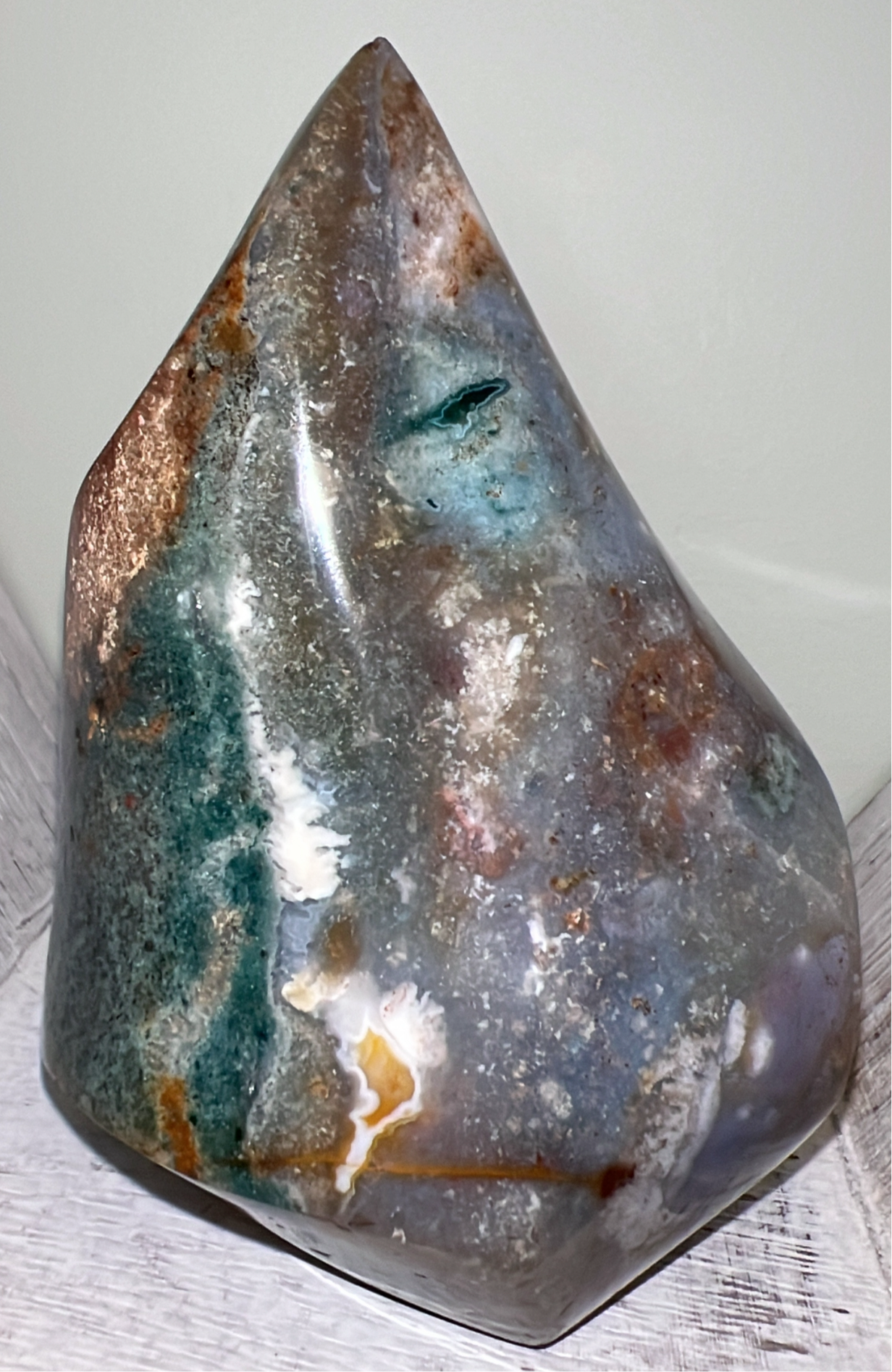 Polished moss agate standing on a white wood surface.