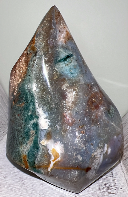 Polished moss agate standing on a white wood surface.