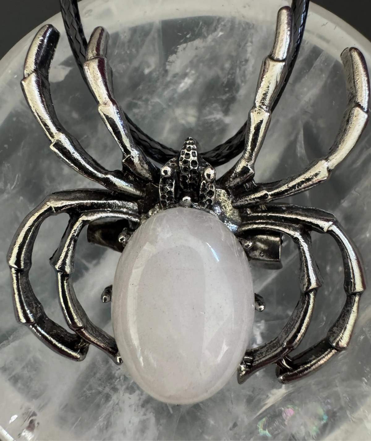 Spider necklace with a pink stone on a rock.
