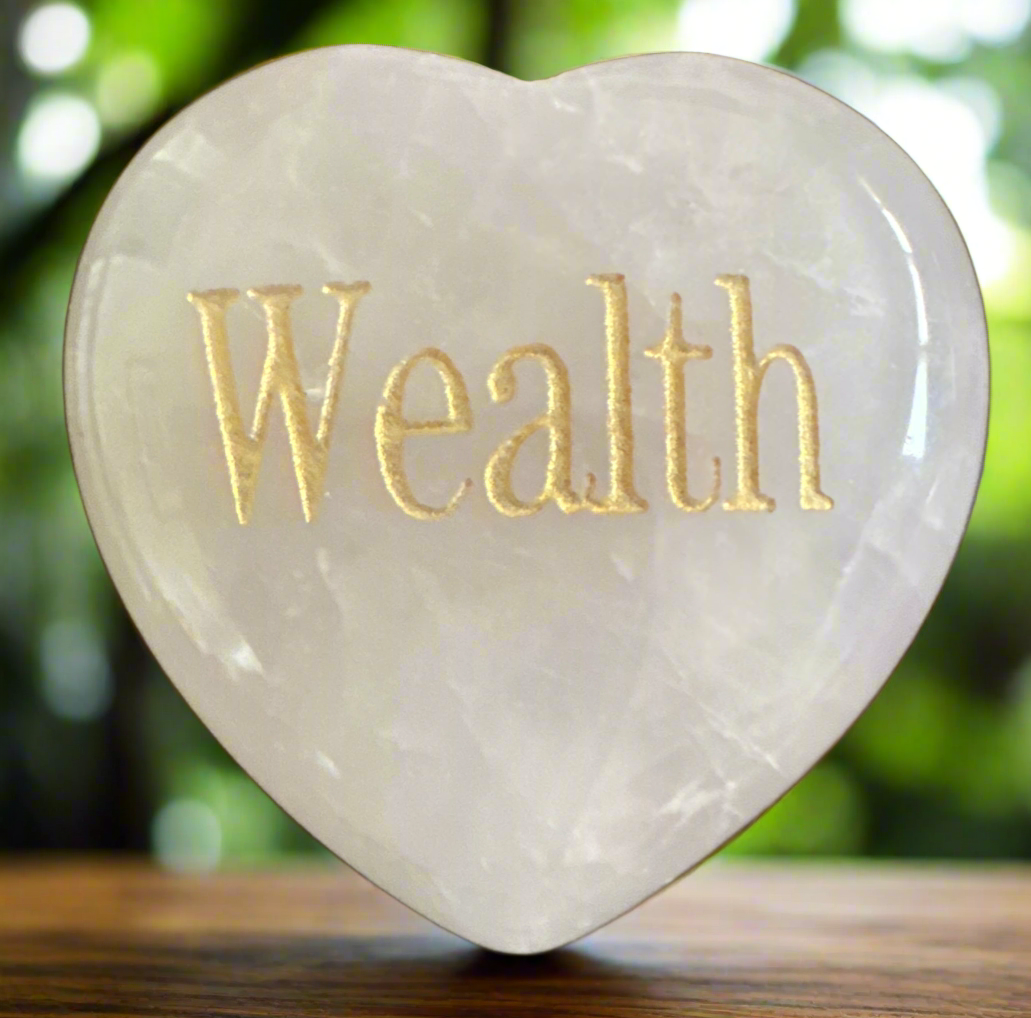 Heart-shaped, white stone with the word "Wealth" engraved in gold.