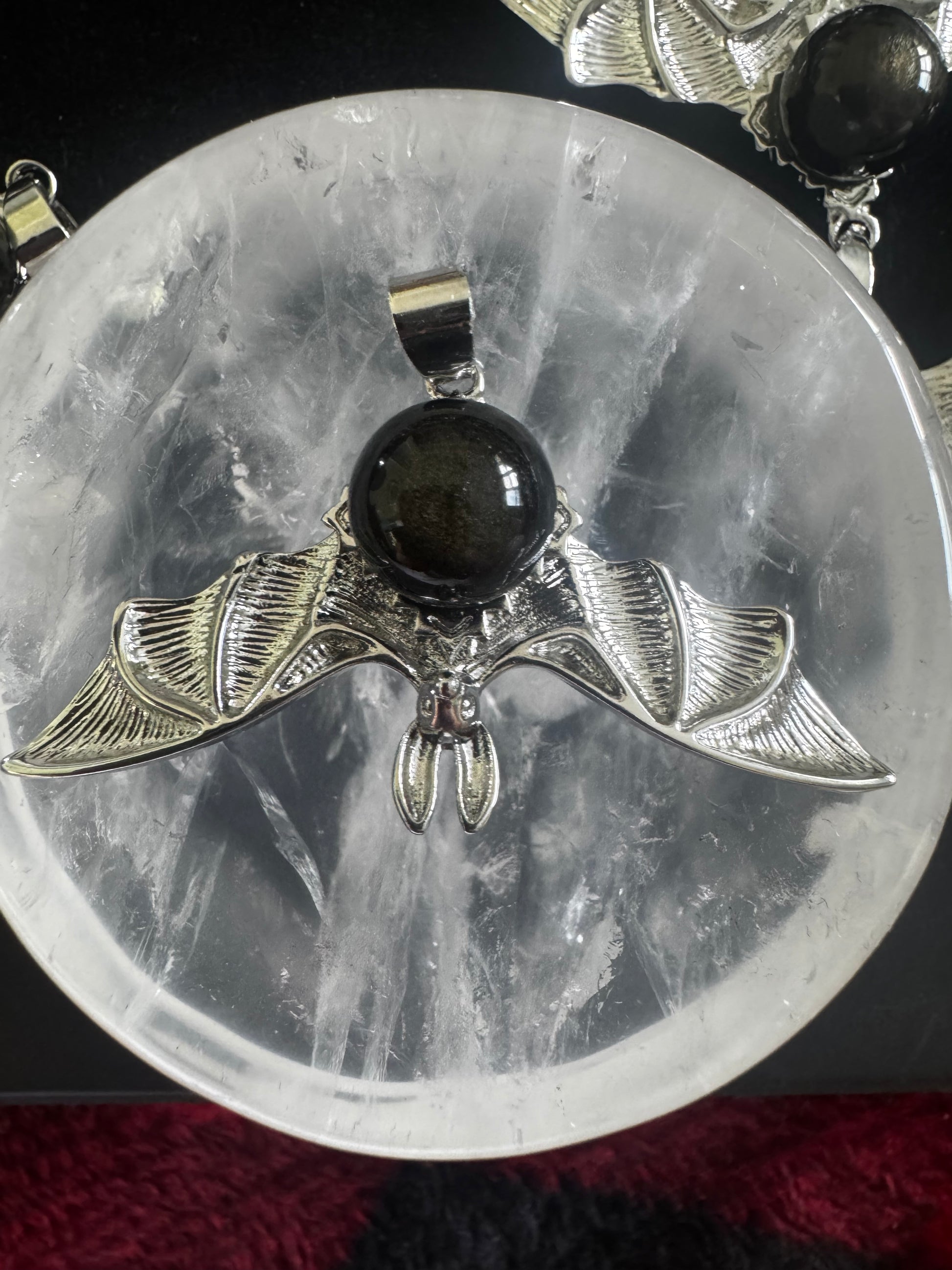 Silver bat pendant with a dark stone, displayed on a clear, round crystal.