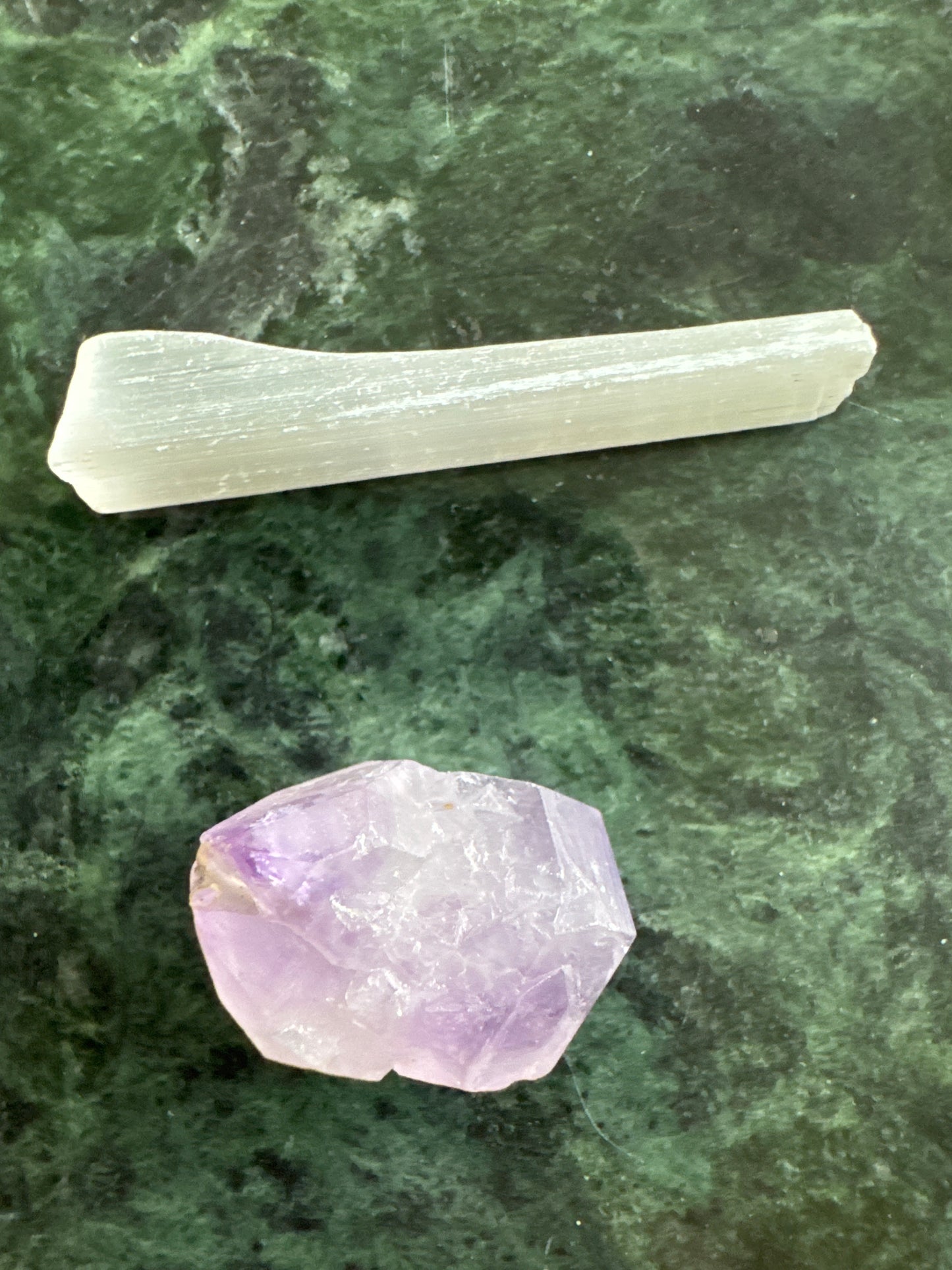 Amethyst crystal and selenite stick on green marble surface.
