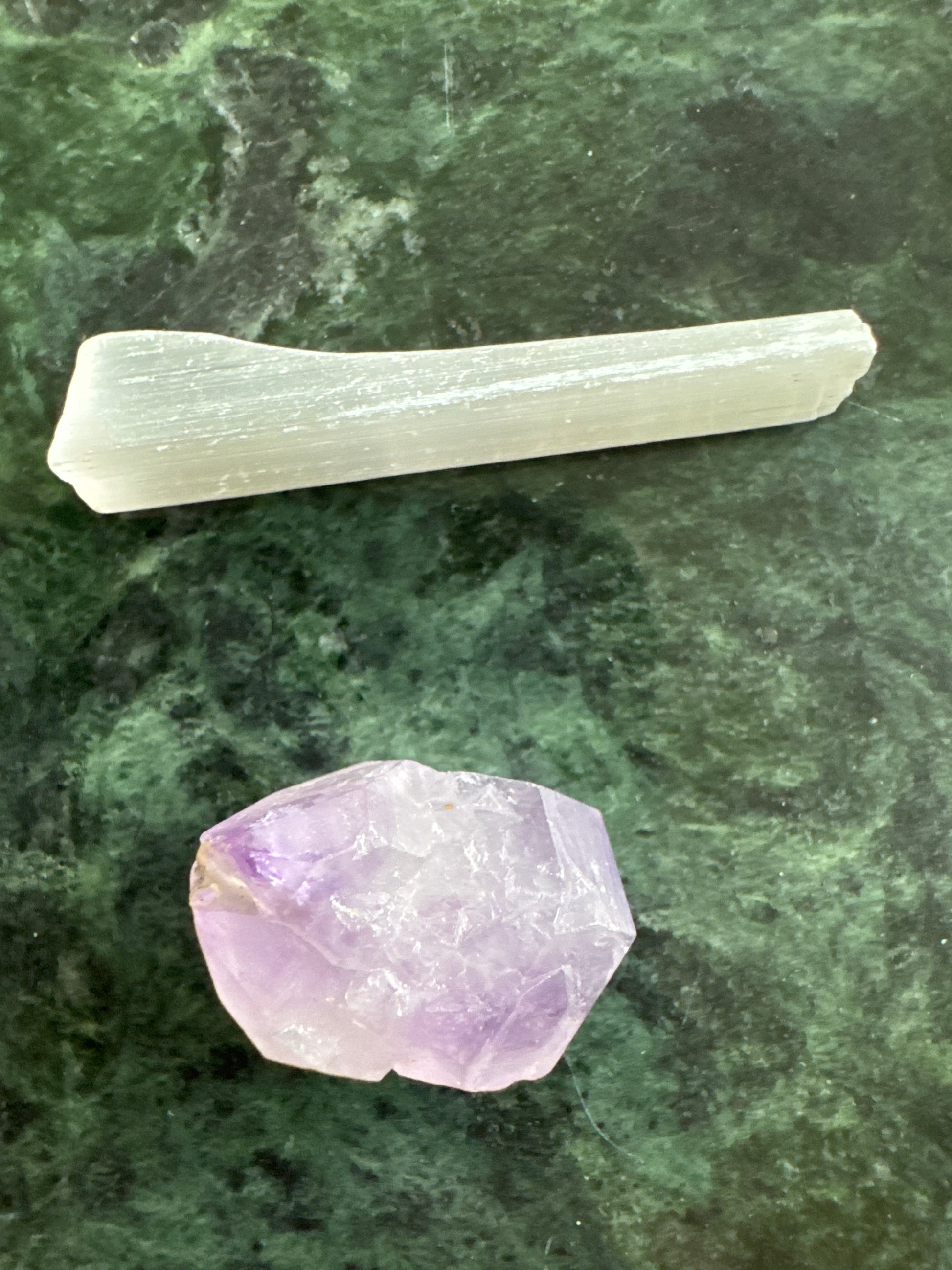 Amethyst crystal and selenite stick on green marble surface.
