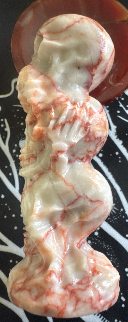 Stack of four carved skull-shaped stones with reddish-orange veining.