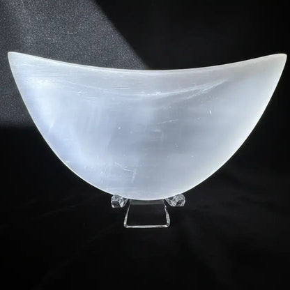 White selenite bowl on a clear stand over a black mat with white designs.