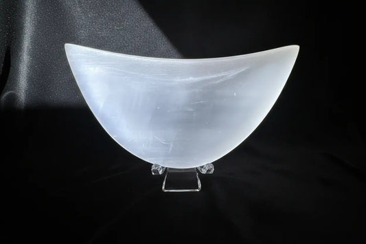 White selenite bowl on a clear stand over a black mat with white designs.