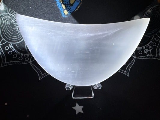 White selenite bowl on a clear stand over a black mat with white designs.
