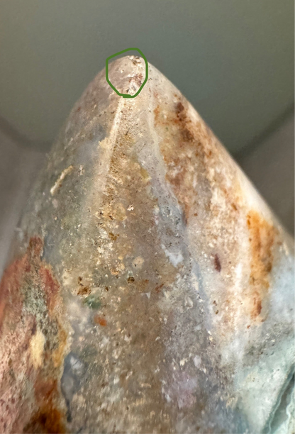 Close-up of a polished, pointed stone with earth tones and a green circle highlighting a flaw.