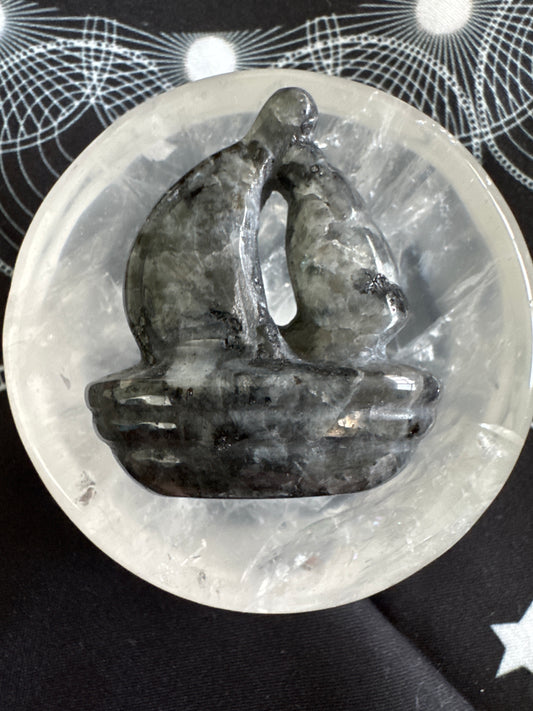 Gray stone sculpture of embracing figures in a clear quartz bowl.