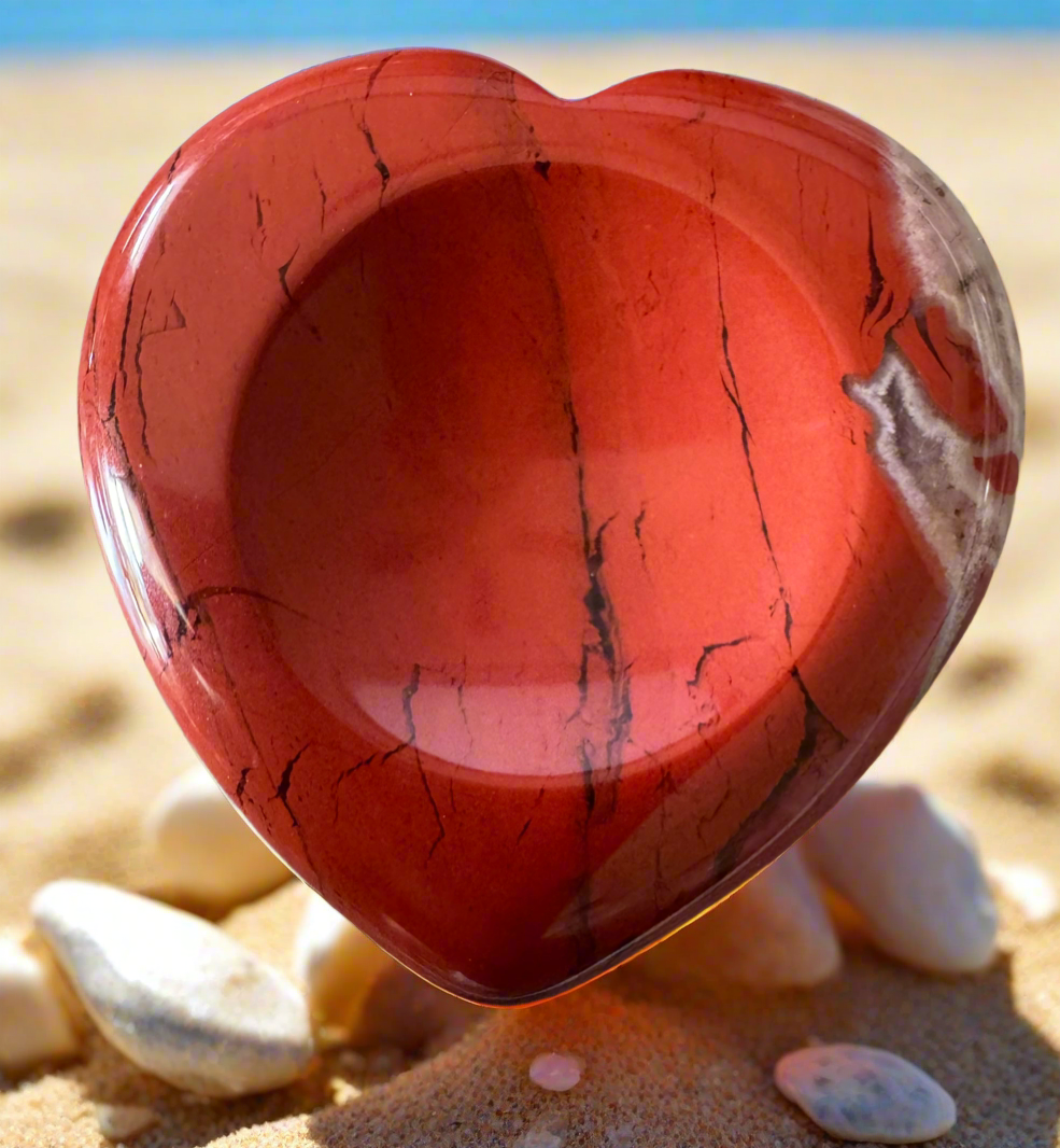 Red jasper heart on a sandy beach.
