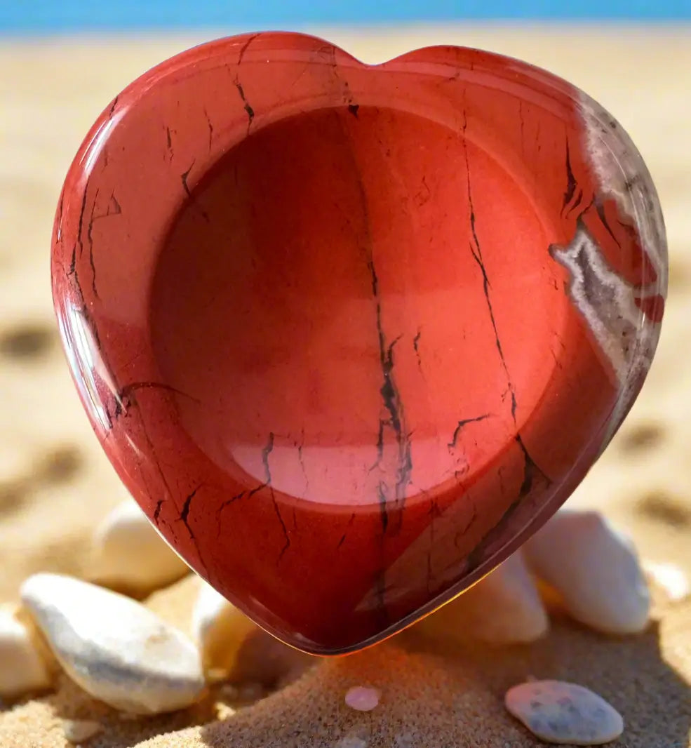 Red jasper heart on a sandy beach.