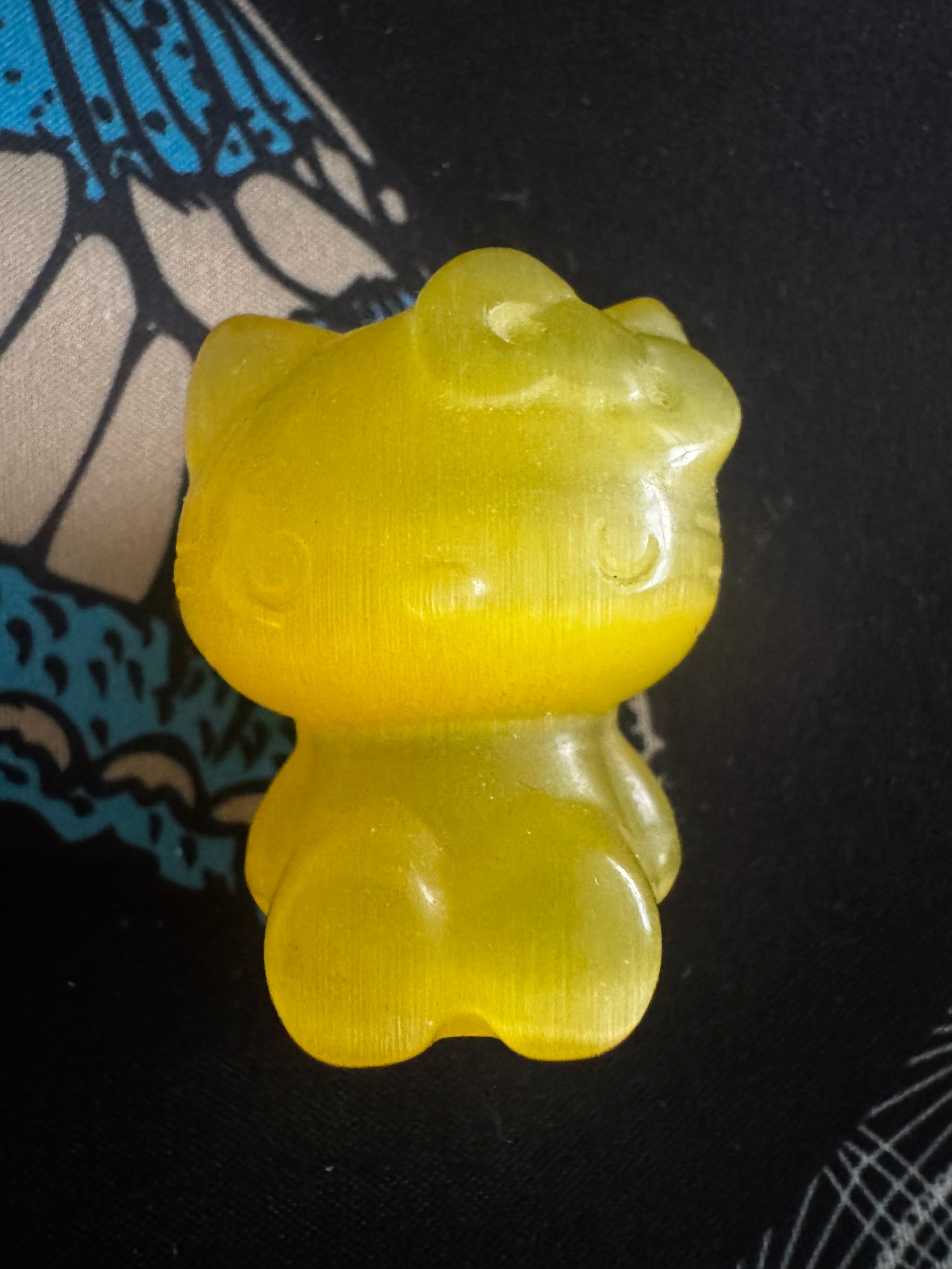Yellow resin Hello Kitty figurine on patterned fabric.
