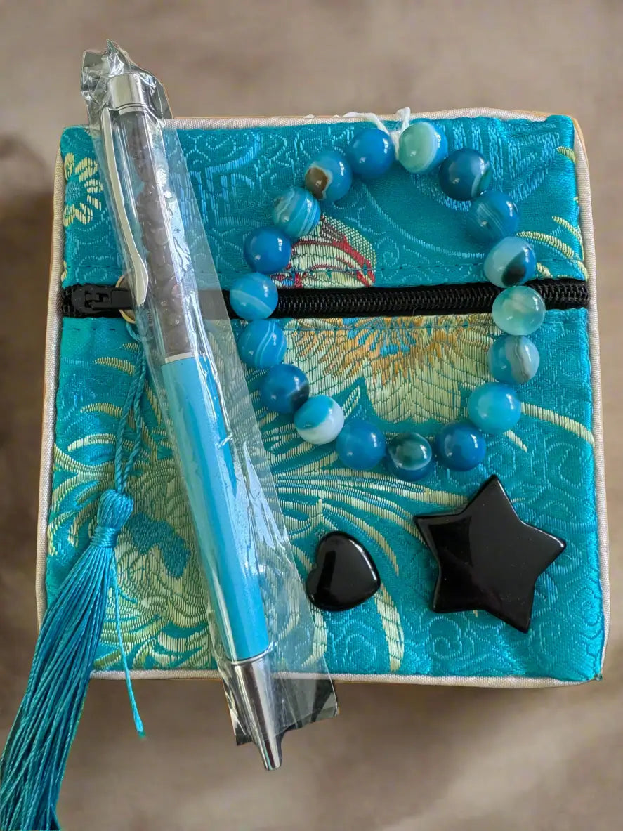 Turquoise brocade box with a beaded bracelet, packaged pen, heart-shaped stone, and star-shaped stone.