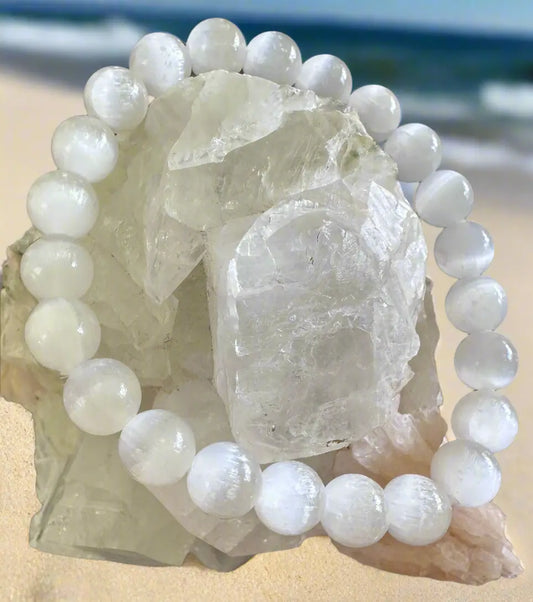 Selenite bead bracelet draped over quartz crystal on beach