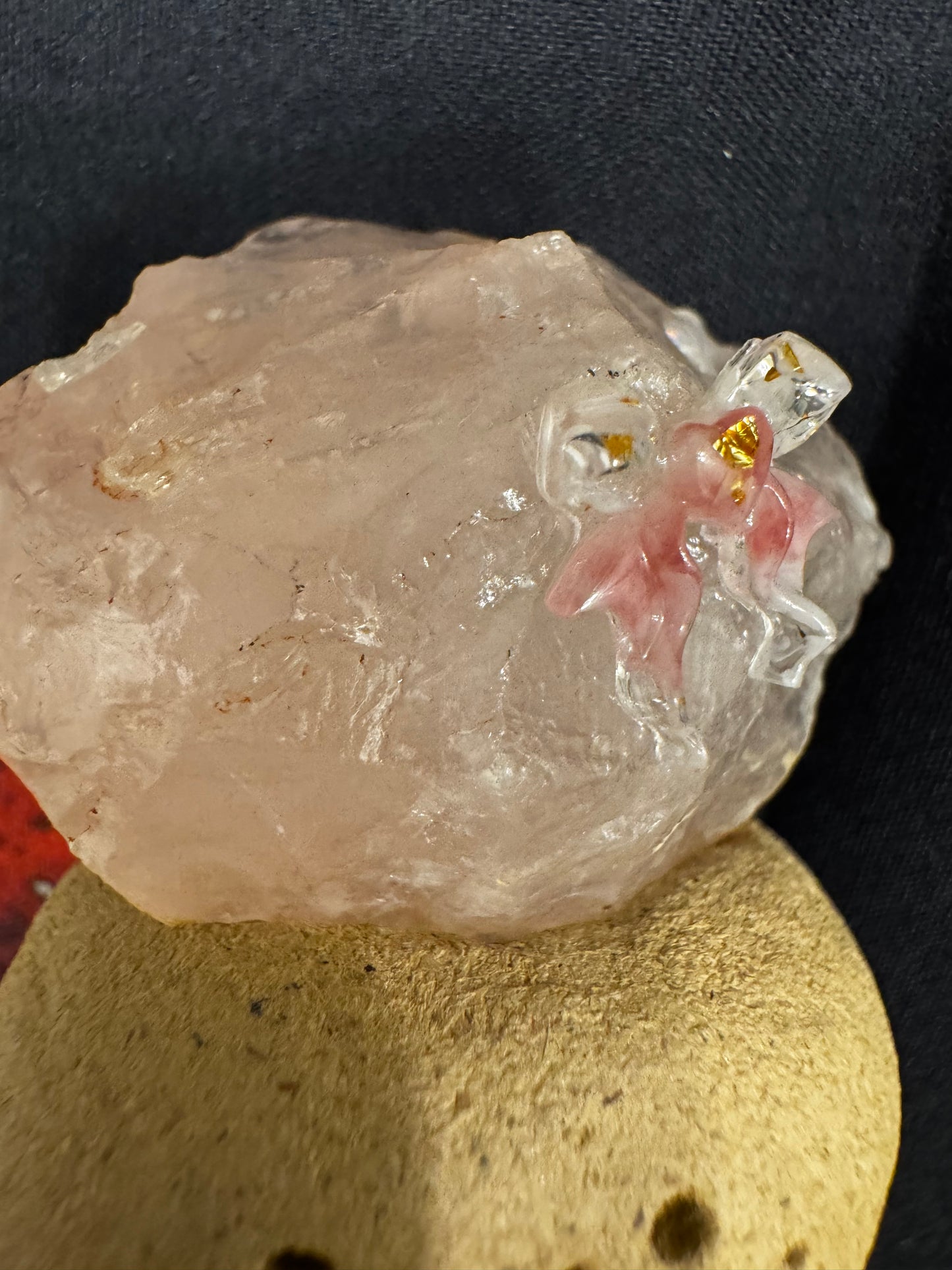 Close-up of a rose quartz crystal with a resin flower on a textured brown stone against a black background.