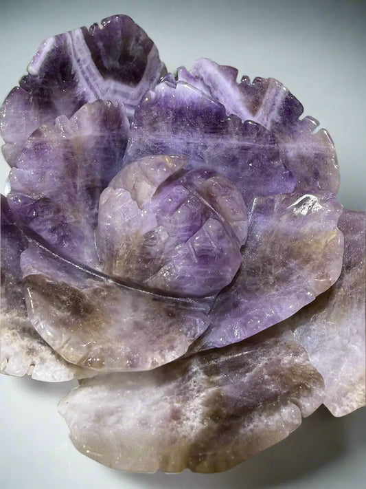 close up amethyst crystal carved to resemble lotus. blossom on a reflective surface
