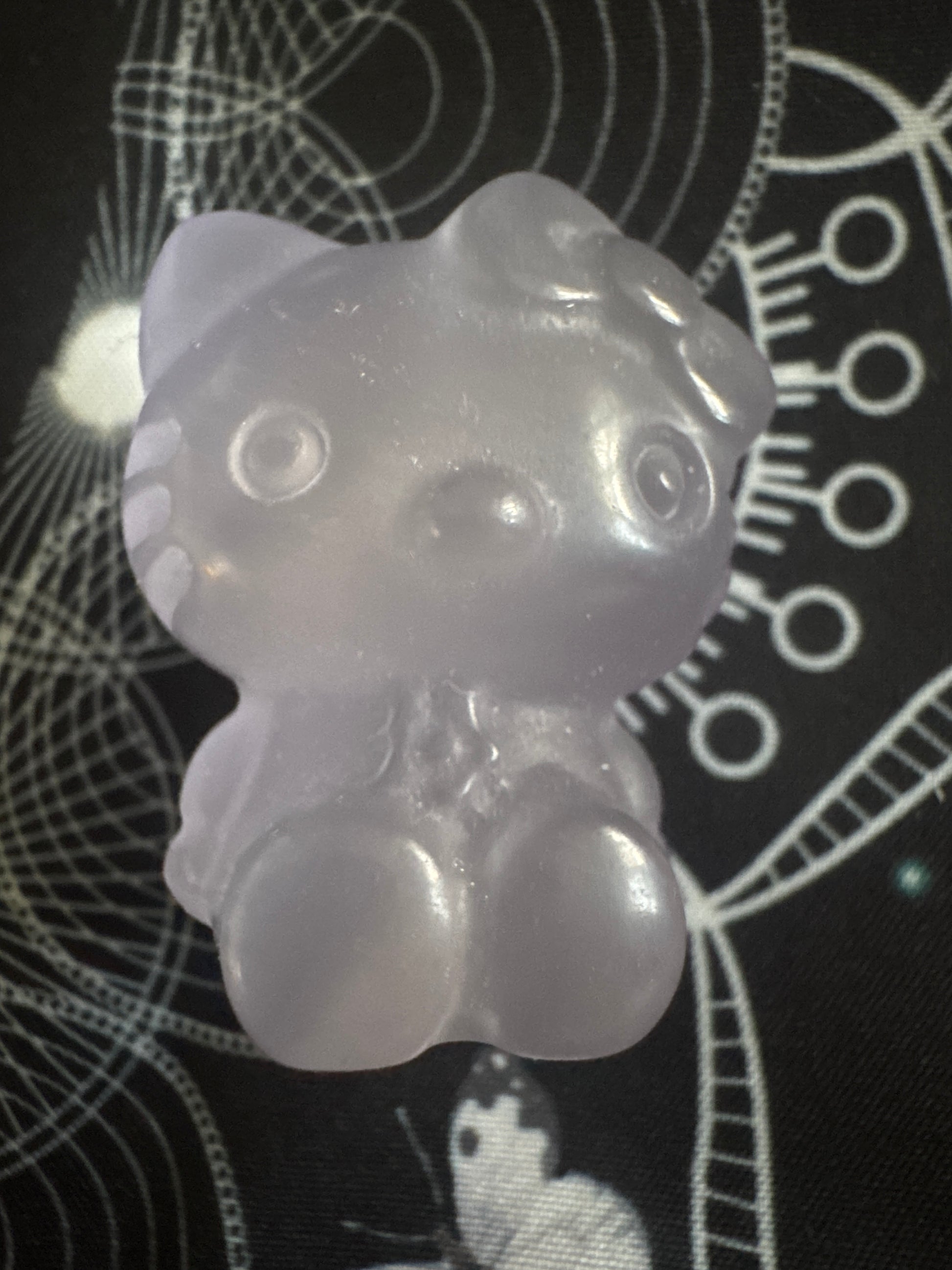 Translucent purple Hello Kitty resin figure on patterned black surface.