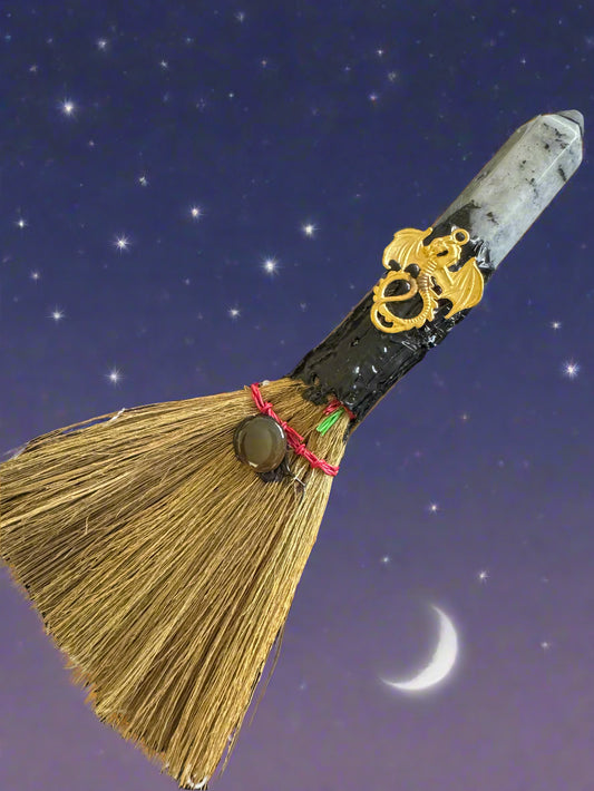 A broom with a labradorite crystal, dragon, and moon.