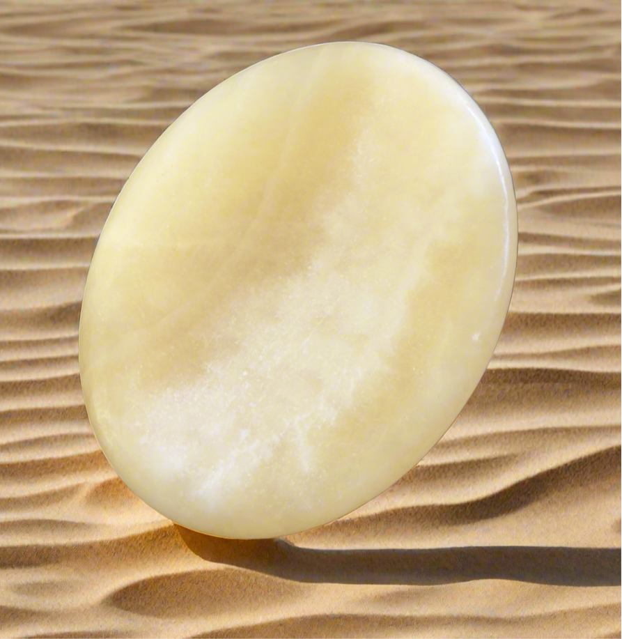 Oval yellow stone casting a shadow on a sandy surface.
