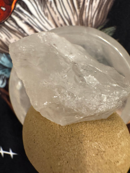 Clear quartz crystal on top of a round, tan rock.