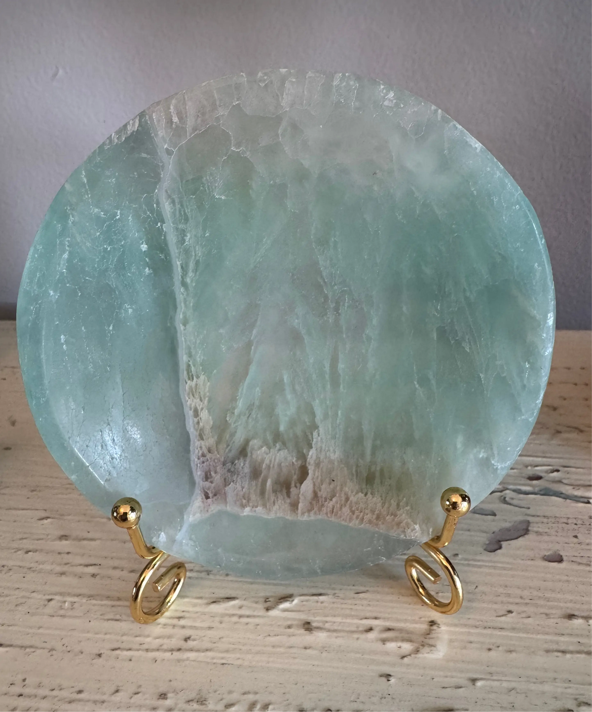 Blue-green circular fluorite plate on gold spiral stand.