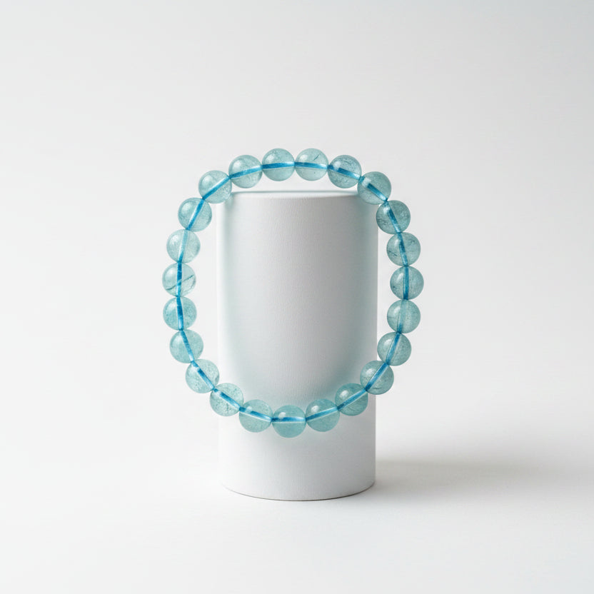 close up looking down at a 9mm aquamarine bead bracelet with blue thread and an off white background