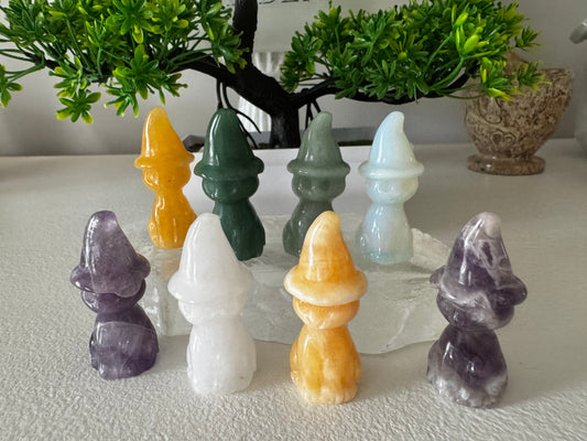 Eight gemstone figurines of gnome-like characters in various colors: yellow, green, light green, pale blue, white, and purple.