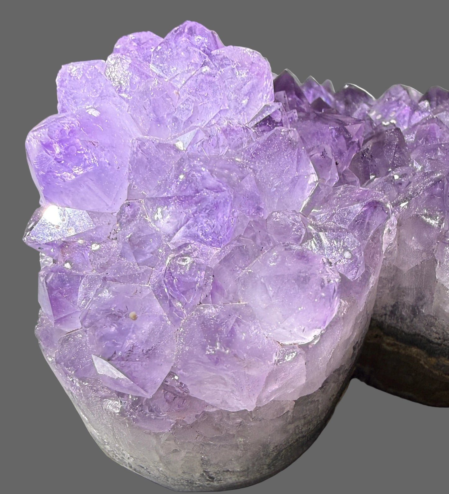 A purple amethyst crystal cluster mounted on a gray stone base, photographed close-up next to a white keyboard.