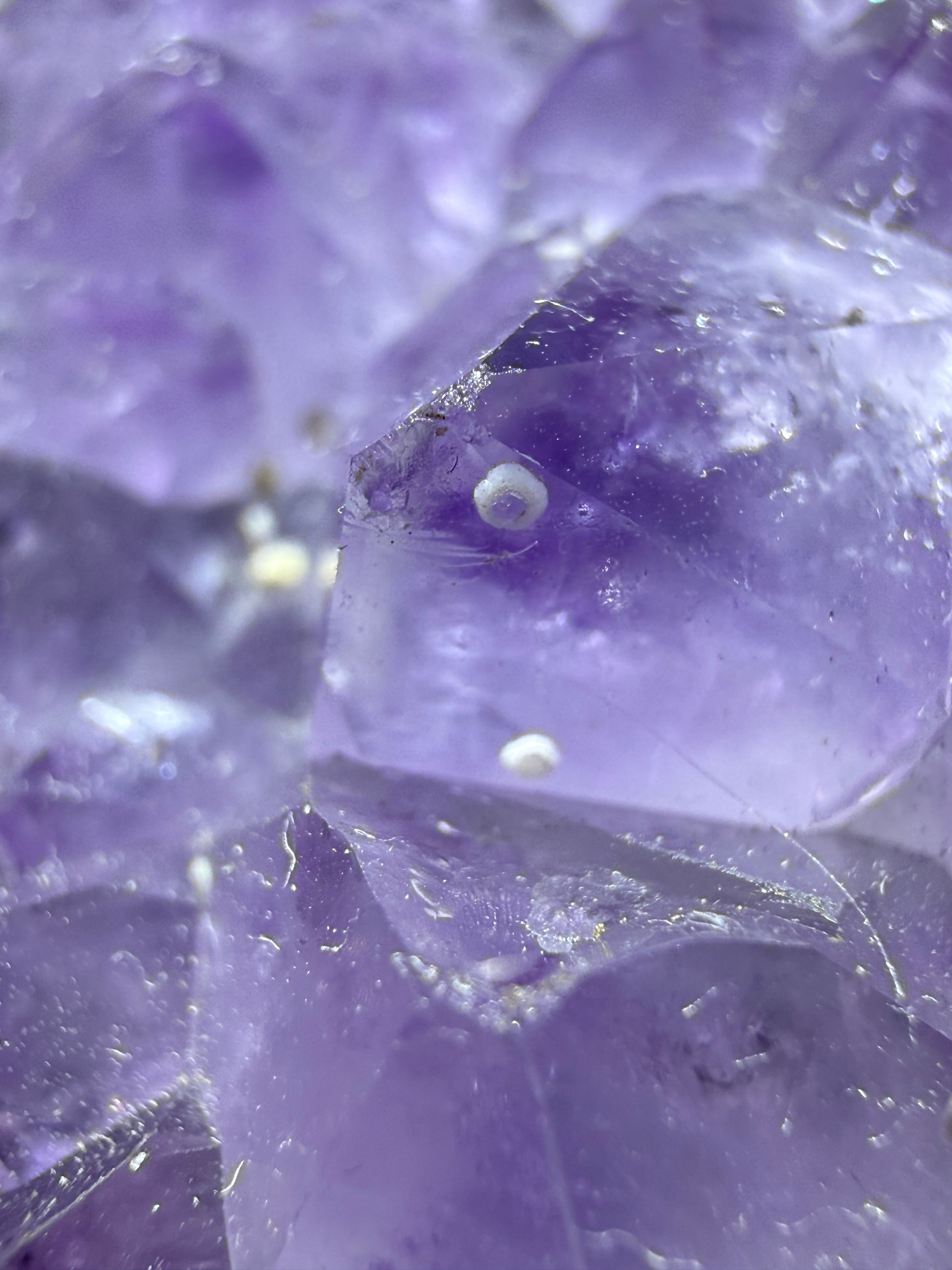 Close-up of translucent purple crystal facets with natural inclusions and a glossy, polished texture. White spots are enhydros - trapped gas or water bubbles