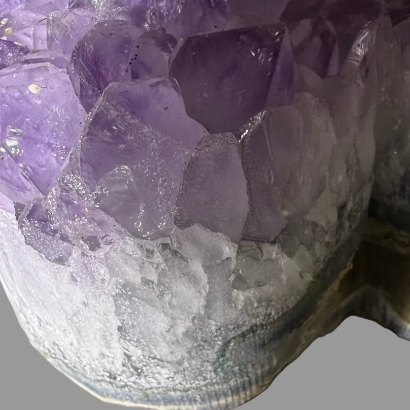 Close-up of an amethyst crystal cluster with translucent purple crystals and a white textured base, photographed against a plain gray background.