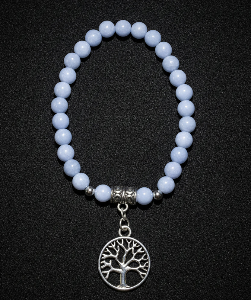 A beaded stretch bracelet featuring  Angelite Crystal  round beads, a silver-toned spacer bead, and a dangling circular tree of life charm displayed on a black fabric 