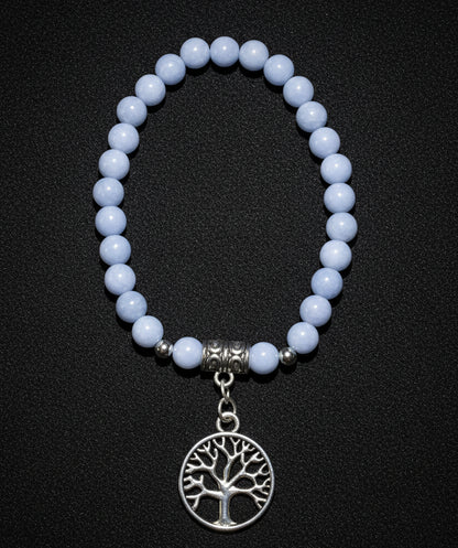 A beaded stretch bracelet featuring  Angelite Crystal  round beads, a silver-toned spacer bead, and a dangling circular tree of life charm displayed on a black fabric 