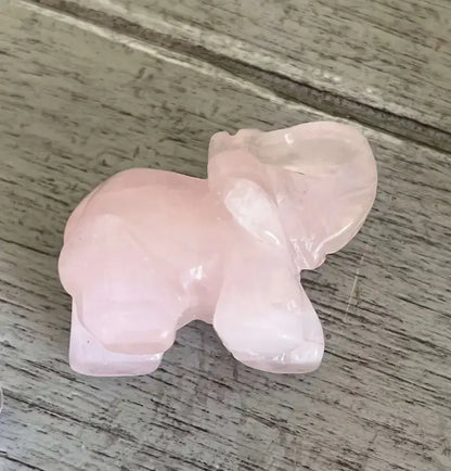 A small carved pink stone elephant figurine, likely made of rose quartz, resting on a weathered gray wooden surface.
