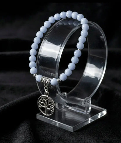 Blue angelite elastic cord bead bracelet with silvery tree of life charm on a stand with a black background