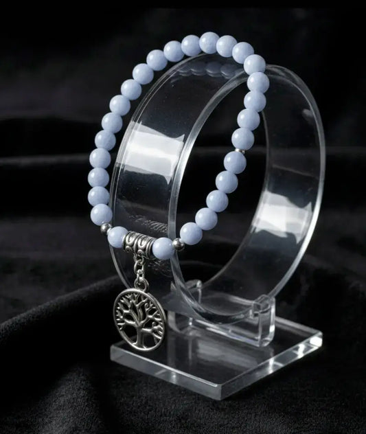 Blue angelite elastic cord bead bracelet with silvery tree of life charm on a stand with a black background