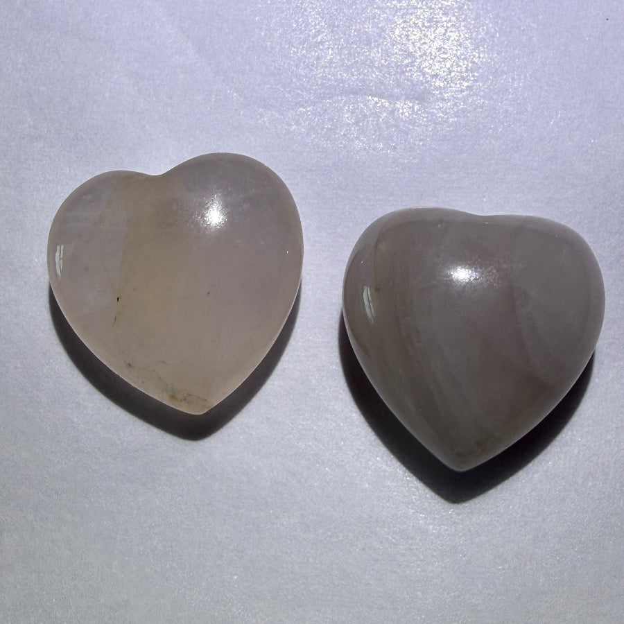 Two rose quartz mini hearts resting on a white surface