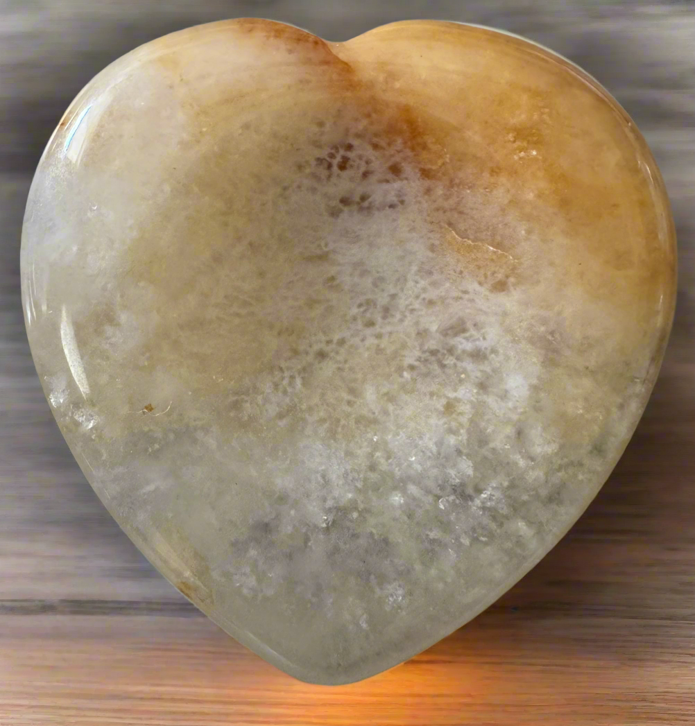 A polished heart-shaped gemstone with a cloudy, yellow and white pattern.